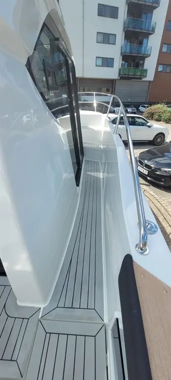 Wide view of a sleek boat deck with striped flooring, railings, and a building backdrop featuring parked cars.